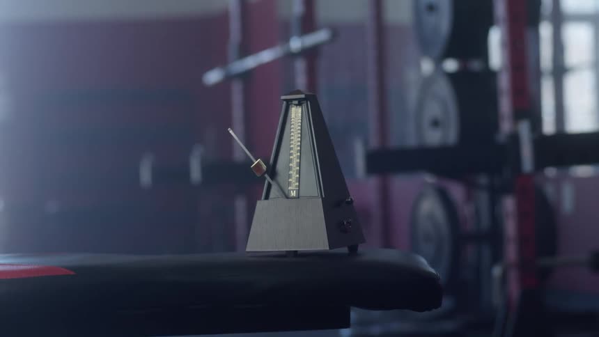 A metronome on a padded bench ticks away in a gym