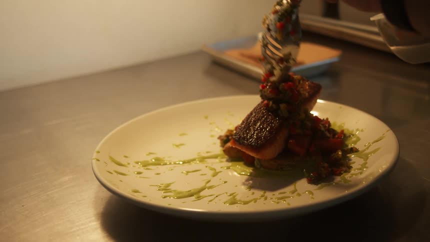 A person with a spoon adding a sauce to a dish on a table