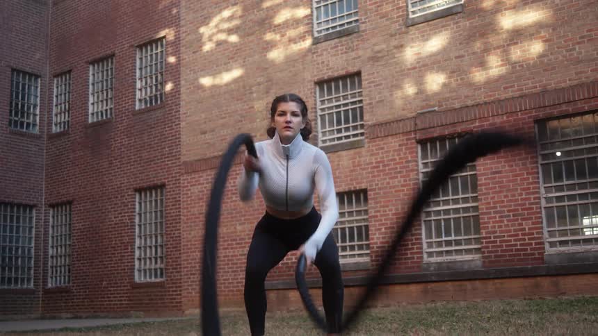 Strong energetic woman works out shaking ropes on the backyard of a building