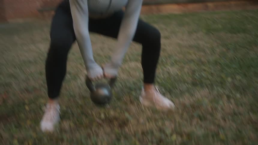 A woman is exercising with a kettle bell outside
