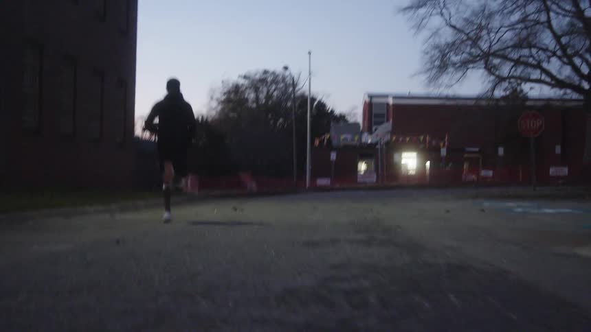 A man sprints behind a building and comes to a stop to rest