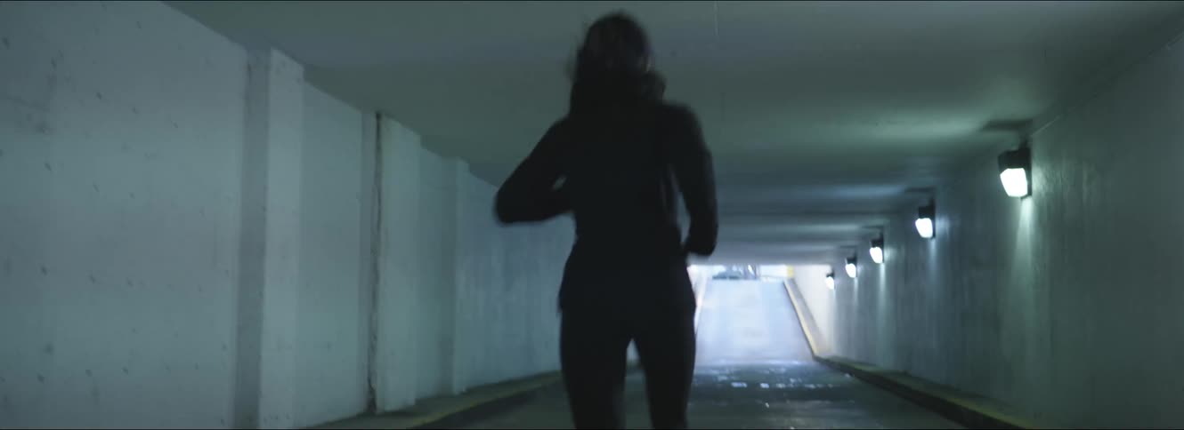 A woman jogging alone through a dark city tunnel