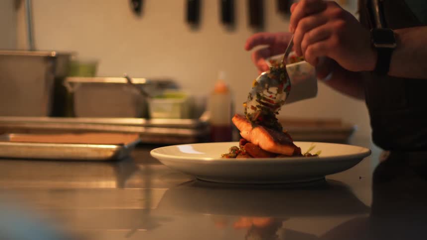 A person putting the final toppings on a piece of meat