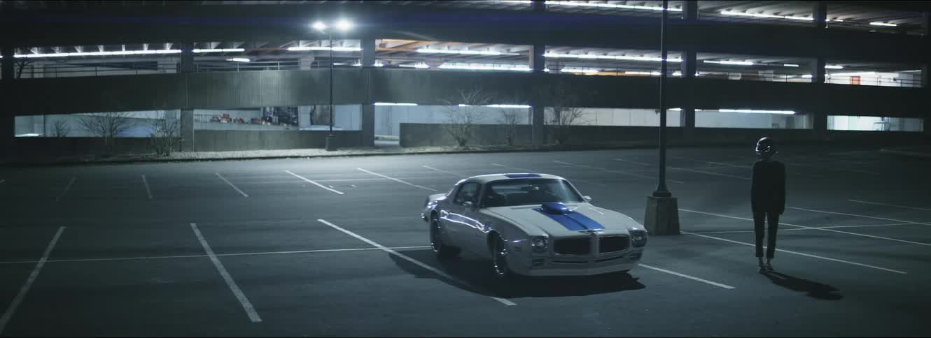 A sports car is parked atop a parking structure at night as a person stands next to it