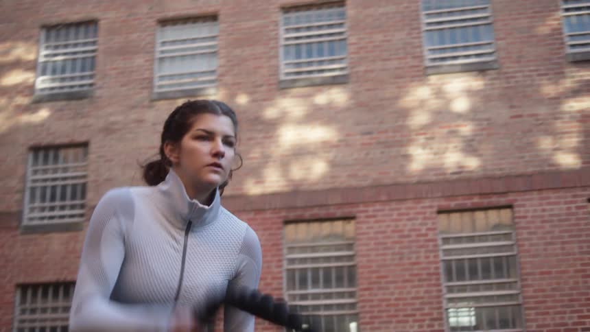 Woman with grey sport shirt black leggings does rope exercises on the grass next to the apartment