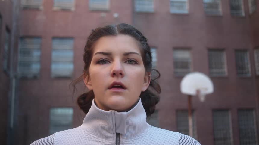 Woman wearing gray sport shirt takes a deep breath in front of apartments