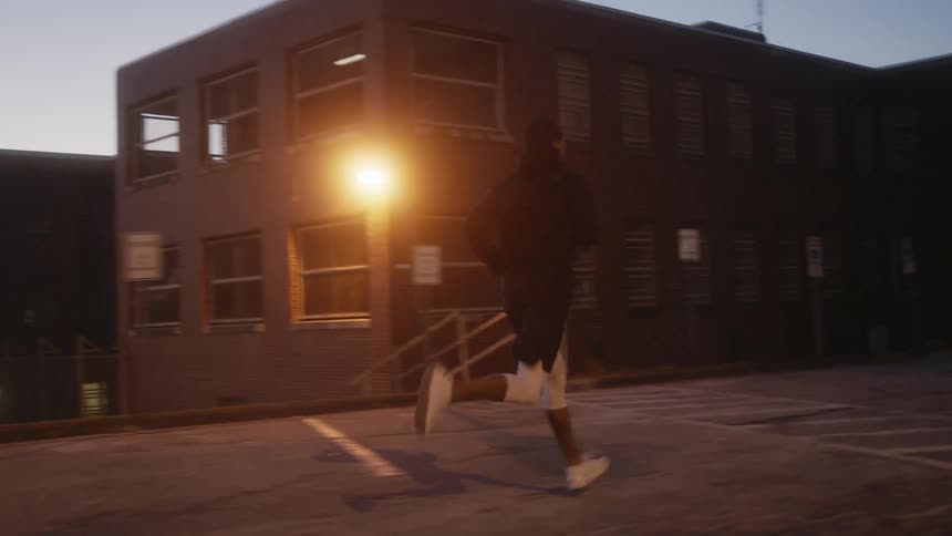 Man with black coat and white jogging pants and sneakers runs in the street at dusk