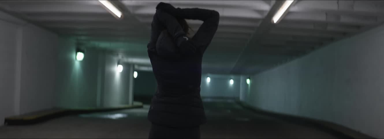 A woman stretches her arms as she walks through a dimly lit building