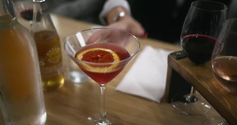 A woman picks up a martini glass from a table filled with alcoholic beverages