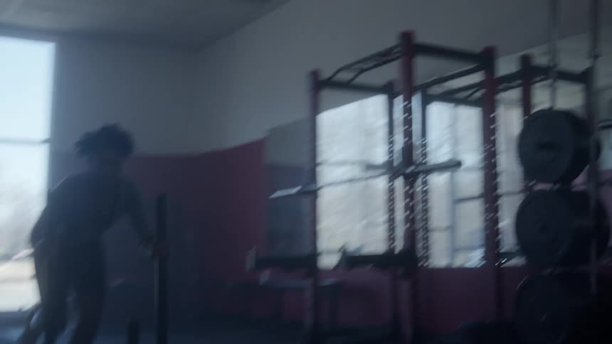 A man pushing equipment in a dark gym while working out