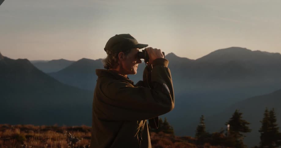 A man looks through binoculars to take in the view at a mountain range