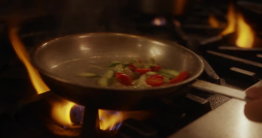 A chef is stir frying vegetables in a pan
