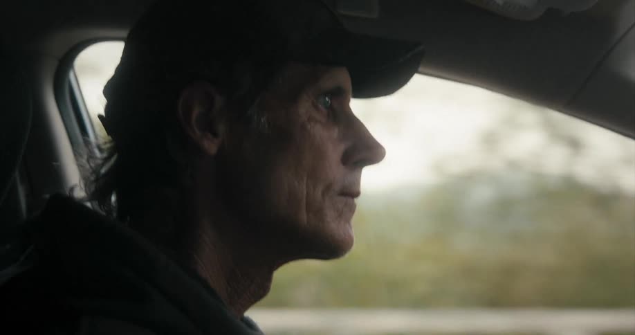 A man drives a vehicle down a rural roadway surrounded by trees