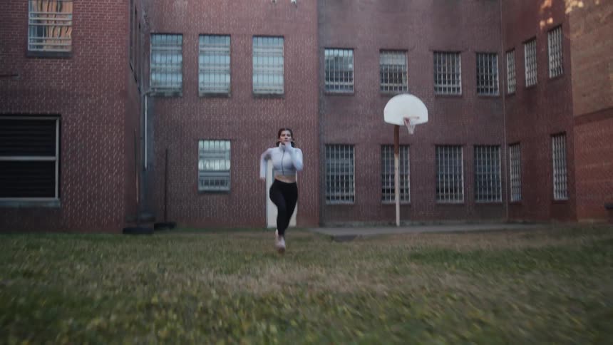 Young woman sprinting on the backyard of a building at morning
