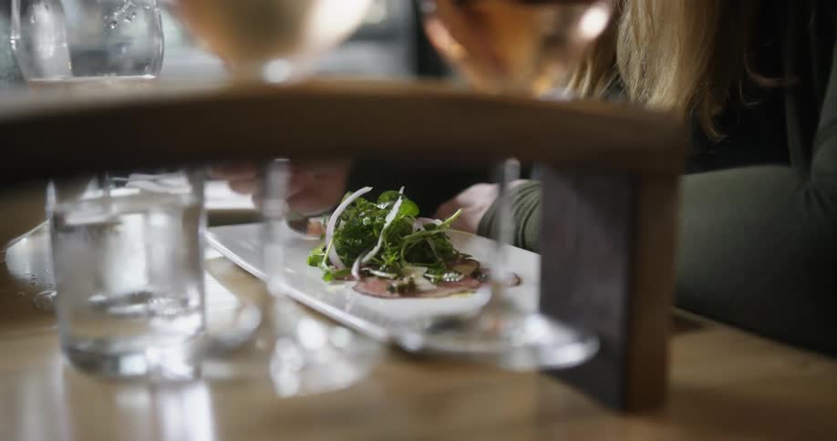 Woman with brown hair and black shirt eats a plate of food in restaurant