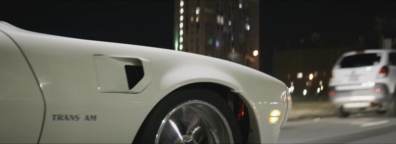 A white trans am passes cars as it travels on a city street at night