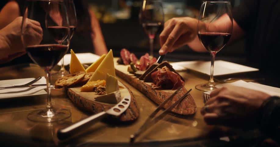 People sit around table eating and drinking wine
