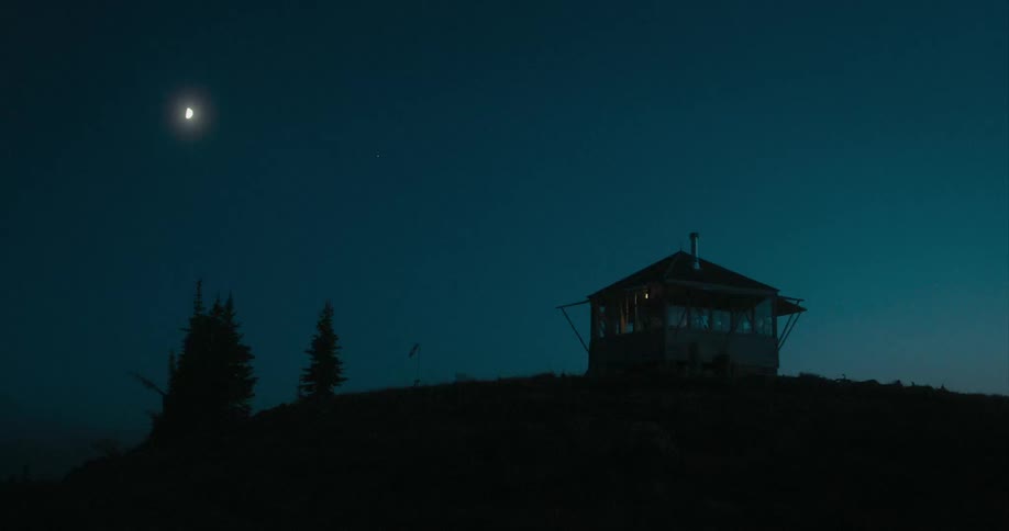 A cabin on a hill with trees with the moon in the sky