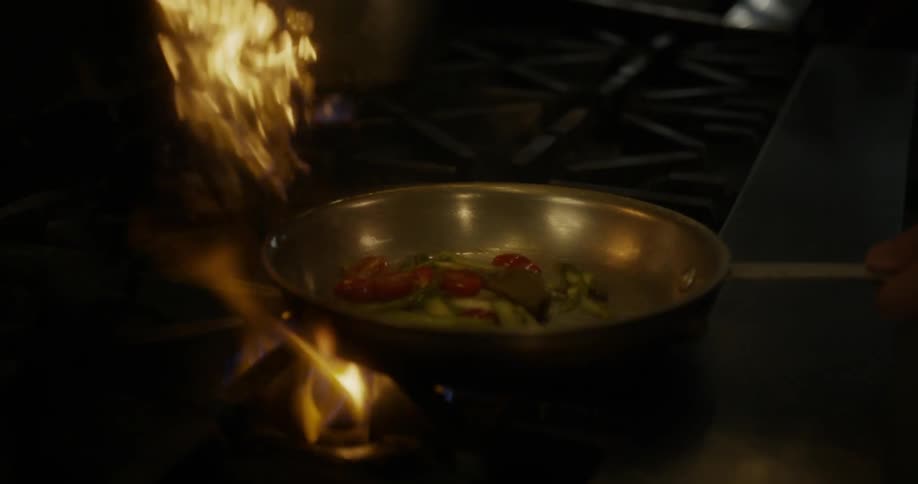 Someone is cooking in a skillet over a gas flame and flambes the food
