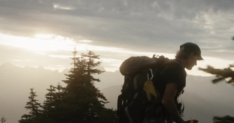 A man wearing a backpack is walking up a hill to a building with mountains on the horizon