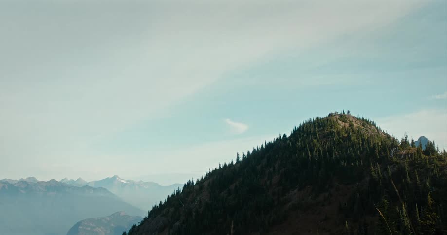 Mountain covered with trees and a mountain range on the horizon