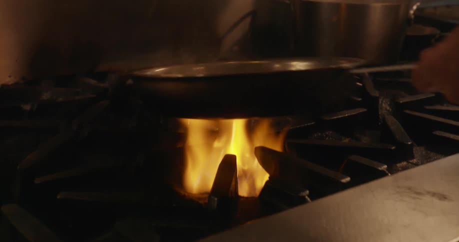 A chef flips food in the pan which gives off a flame