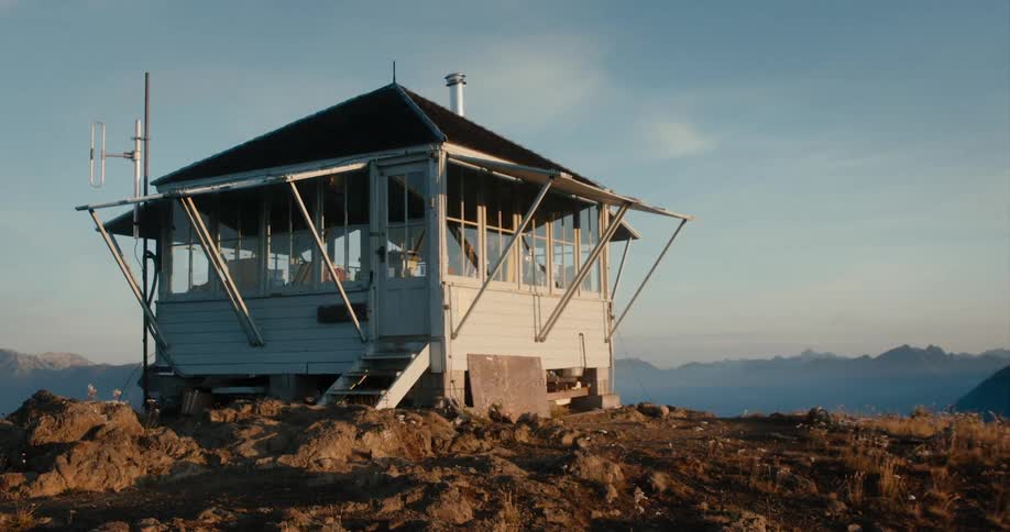 Fire lookout atop a mountain near a mountain range at sunset