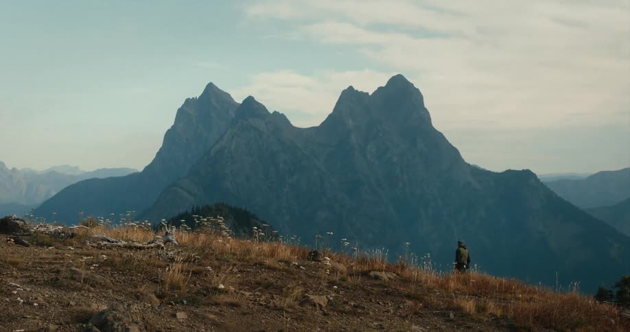 A person walking on a hill with a mountain range the sky and clouds in the background