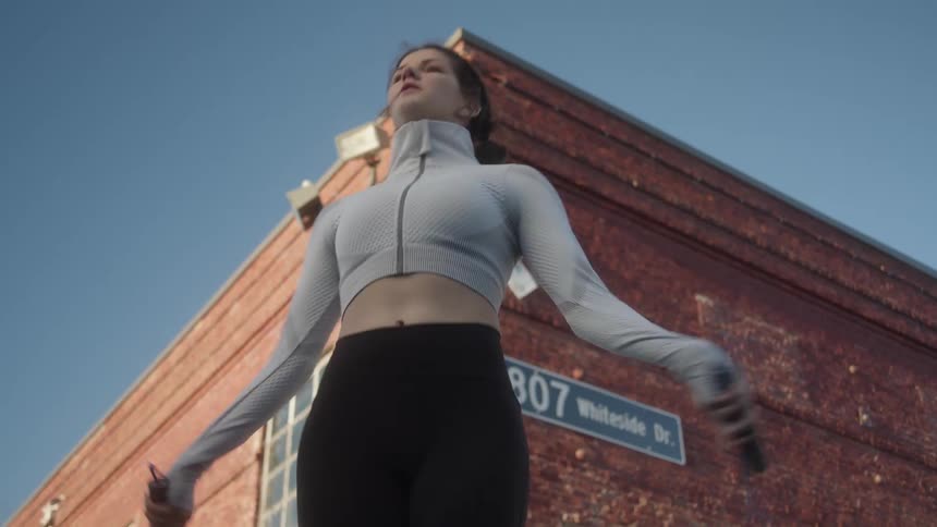Woman jumps rope near corner of red brick building with address sign attached under clear blue sky
