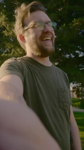 A man laughs as he records a video of himself in a park