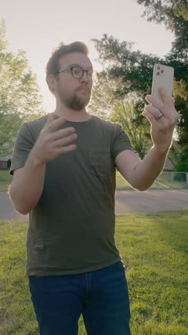 Man standing outdoors uses smartphone for video call at sunset