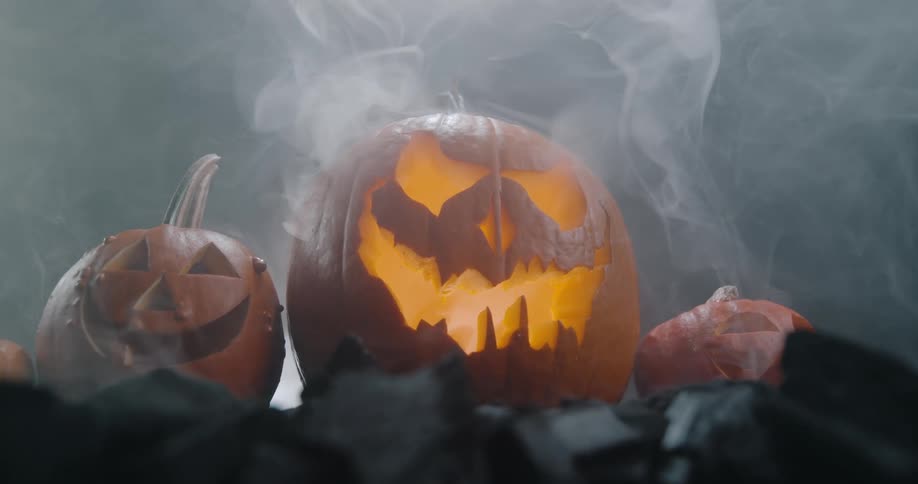 A halloween arrangement with evil pumpkins and rising smoke in a dark studio environment