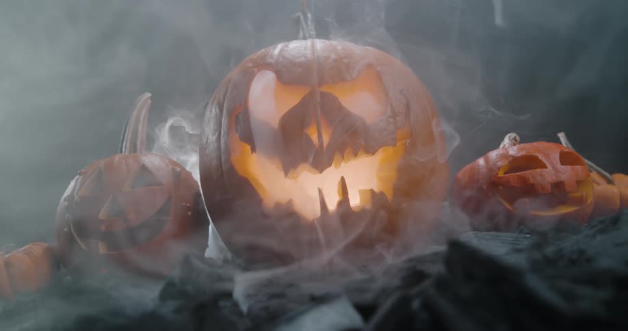 Carved jack o lanterns sit on a bed of rocks as smoke swirls around them