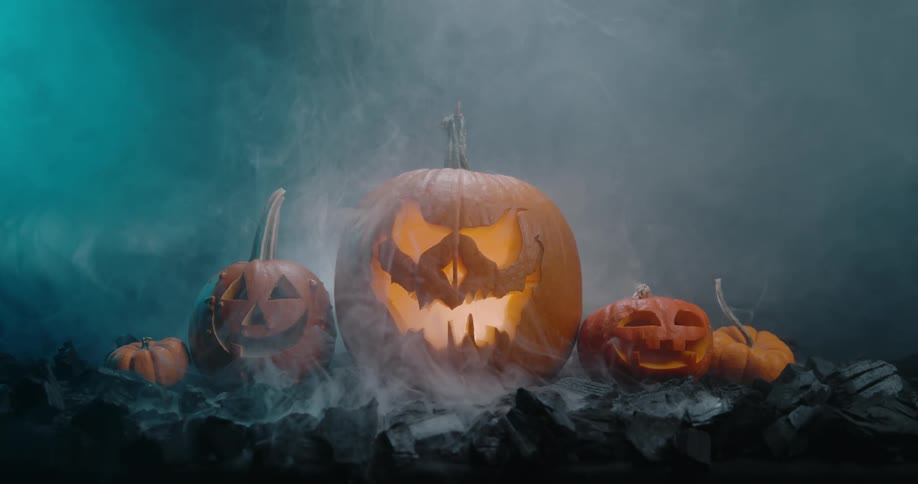 Lit jack olantern sits in middle of carved pumpkins on foggy dark ground at night
