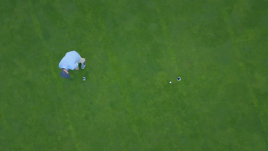 A golfer putts on the green putting the ball in the hole