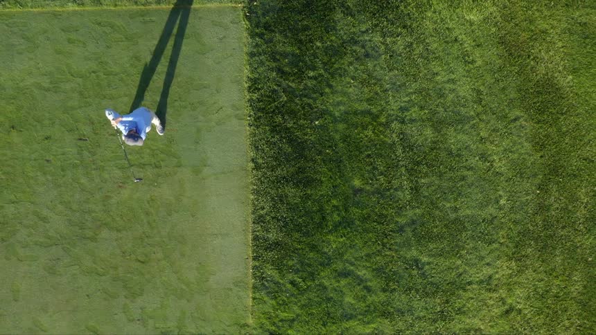 Golfer swings at ball driving it over grass