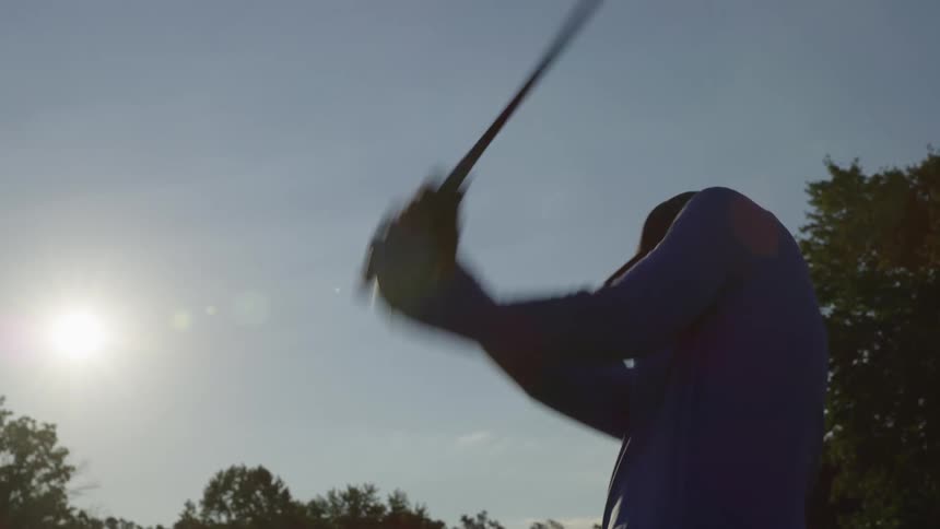 A man swings a golf club and looks to see where the ball landed