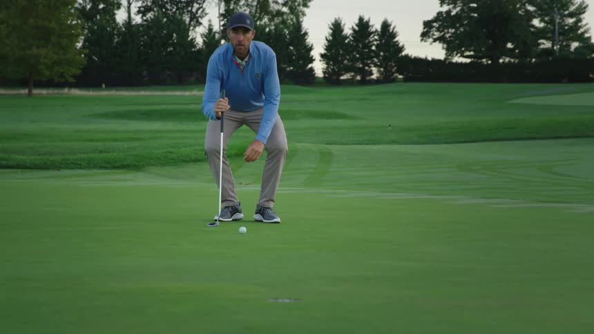 A golfer squats down to get a better look at the hole and ball before putting