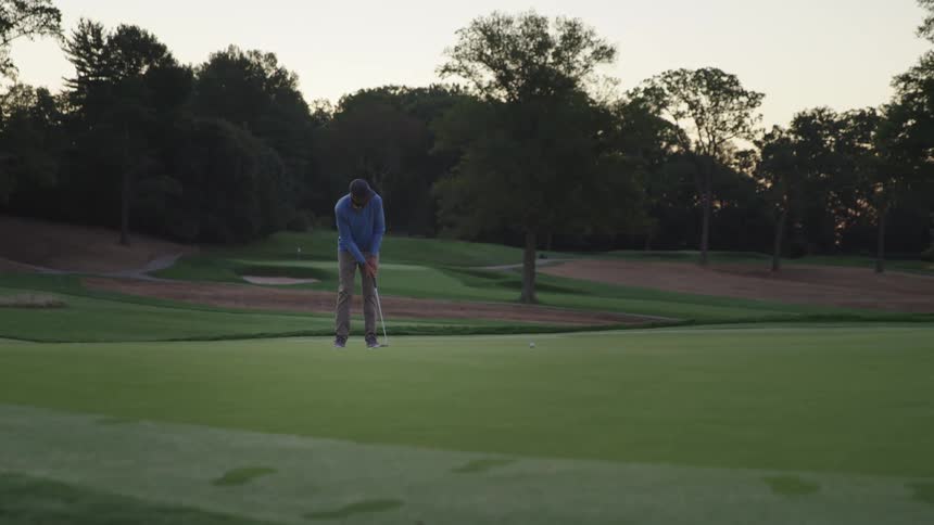 Golfer sinks putt on dimly lit day