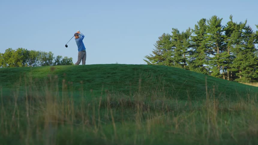 A man swings a club as he hits a ball while golfing