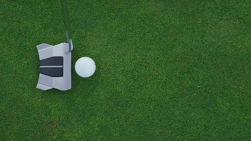 A putter swings at a golf ball on the green