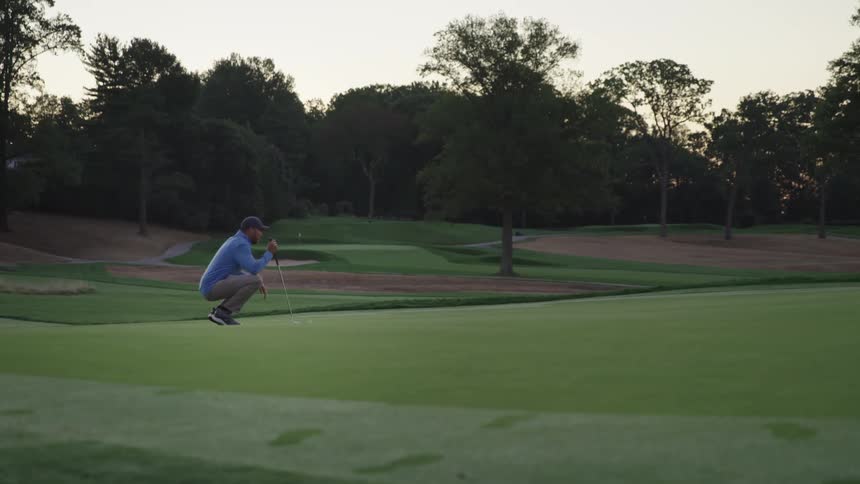 A man on a golf course is studying his next shot in the early morning