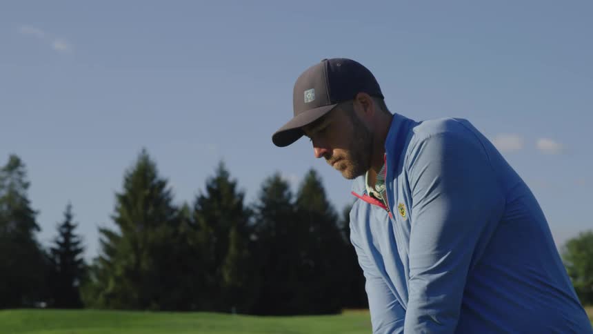 A man aims and takes a swing on a golf course