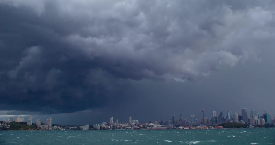 Storm clouds with lightning loom over a large metropolis in the distance on the far side of a body of water