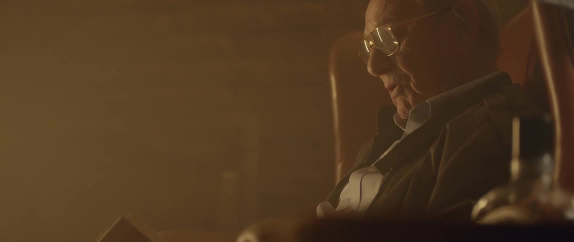 A man sitting in a chair reads a book aloud