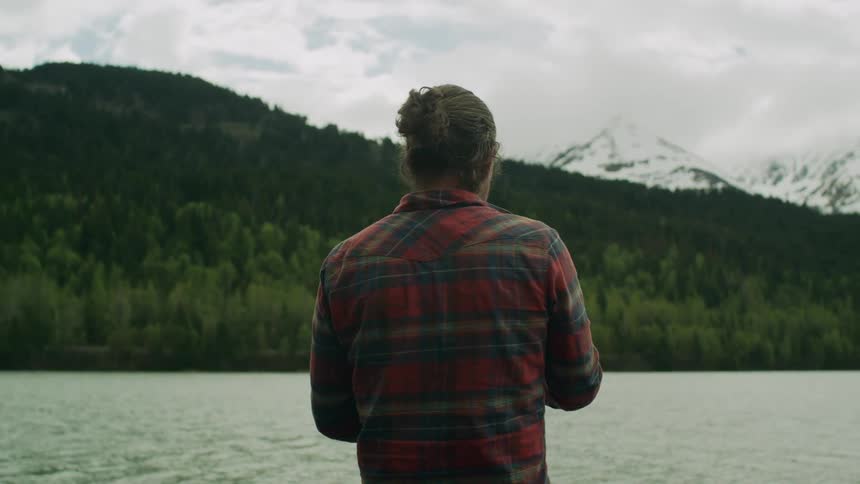 A man in a plaid flannel smiles as he stands next to a large lake