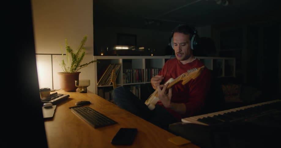 A man in a room with headphone sitting at a desk with a wall in the background