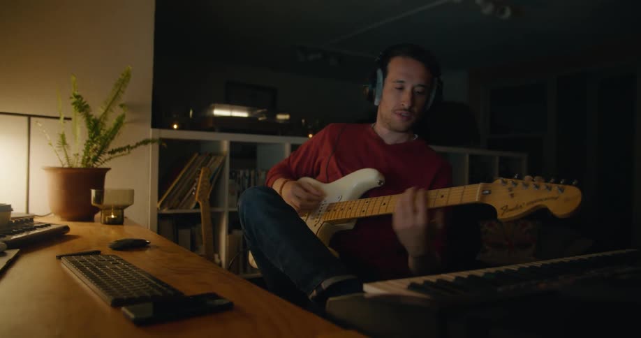 A man in a room with headphone sitting at a desk with a wall in the background