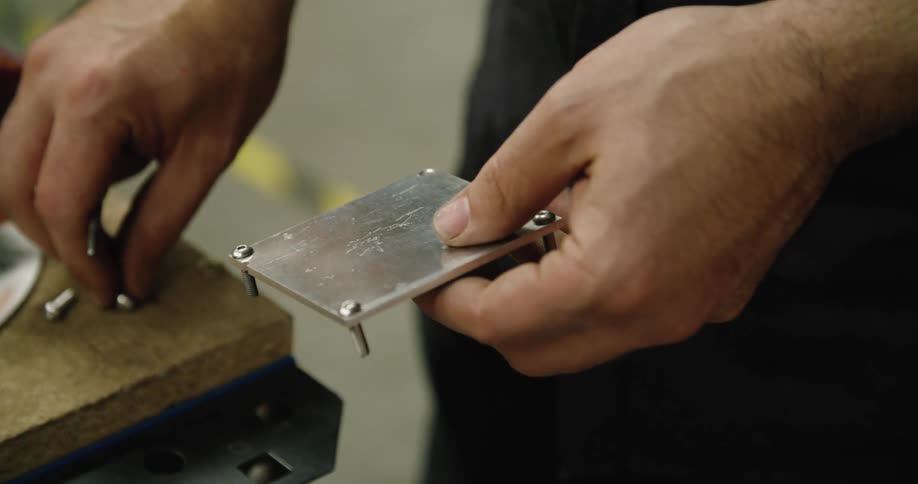 Standing near particle board topped bench man slots screws into small metal square
