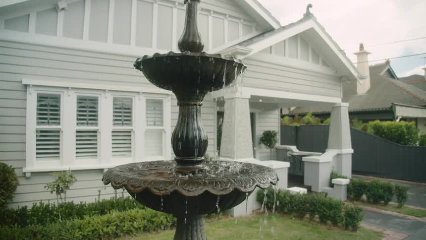 A quaint home has a well manicured yard and a water fountain in the front yard